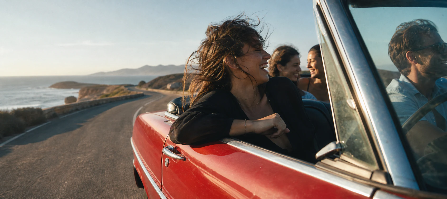 Friends driving a vintage red convertible on a coastal road