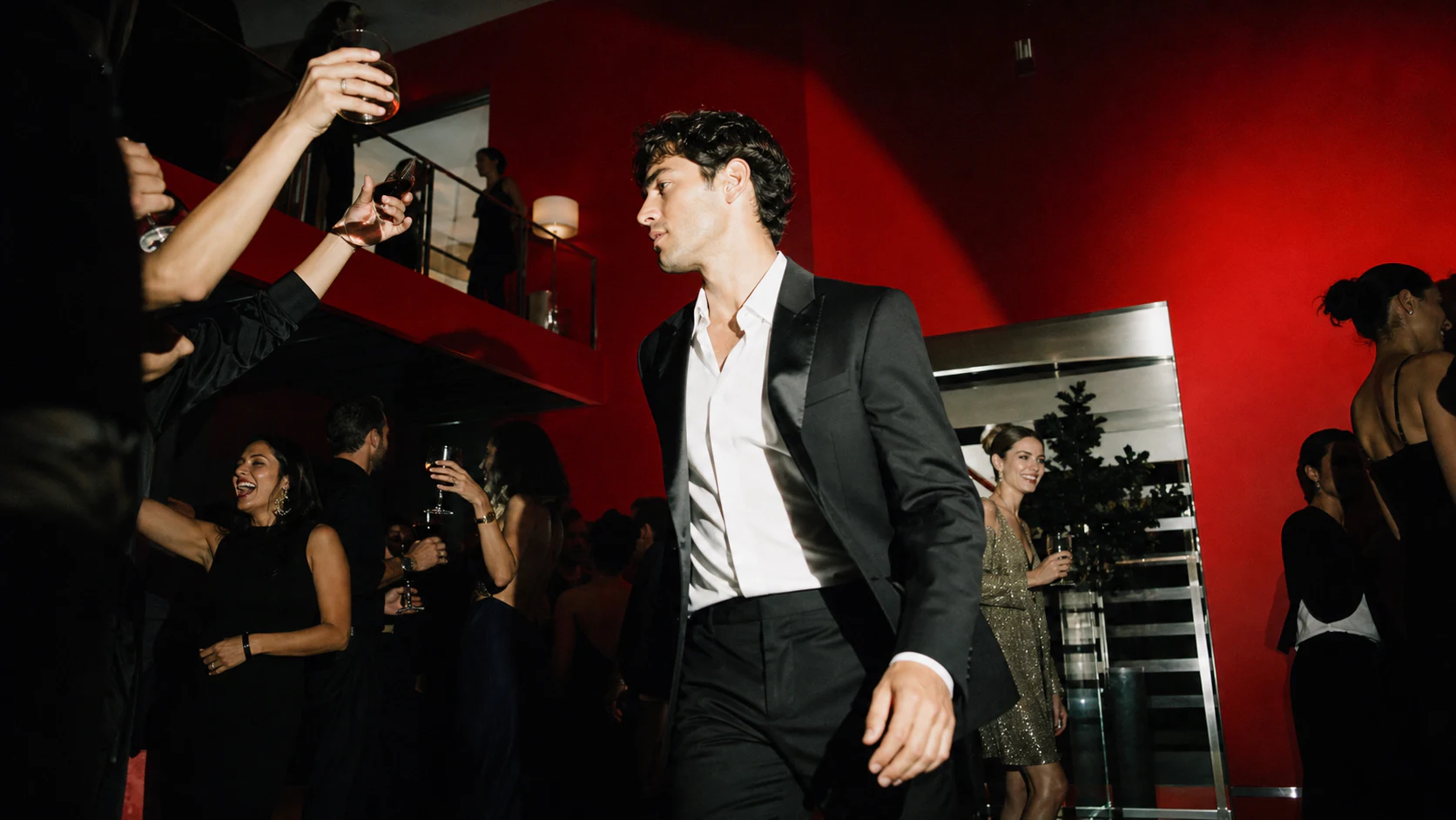 Guests in evening wear crossing a vivid red party room